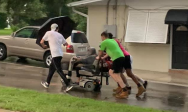 Quatro jovens empurram uma senhora idosa para casa depois que sua scooter elétrica quebrou na chuva torrencial